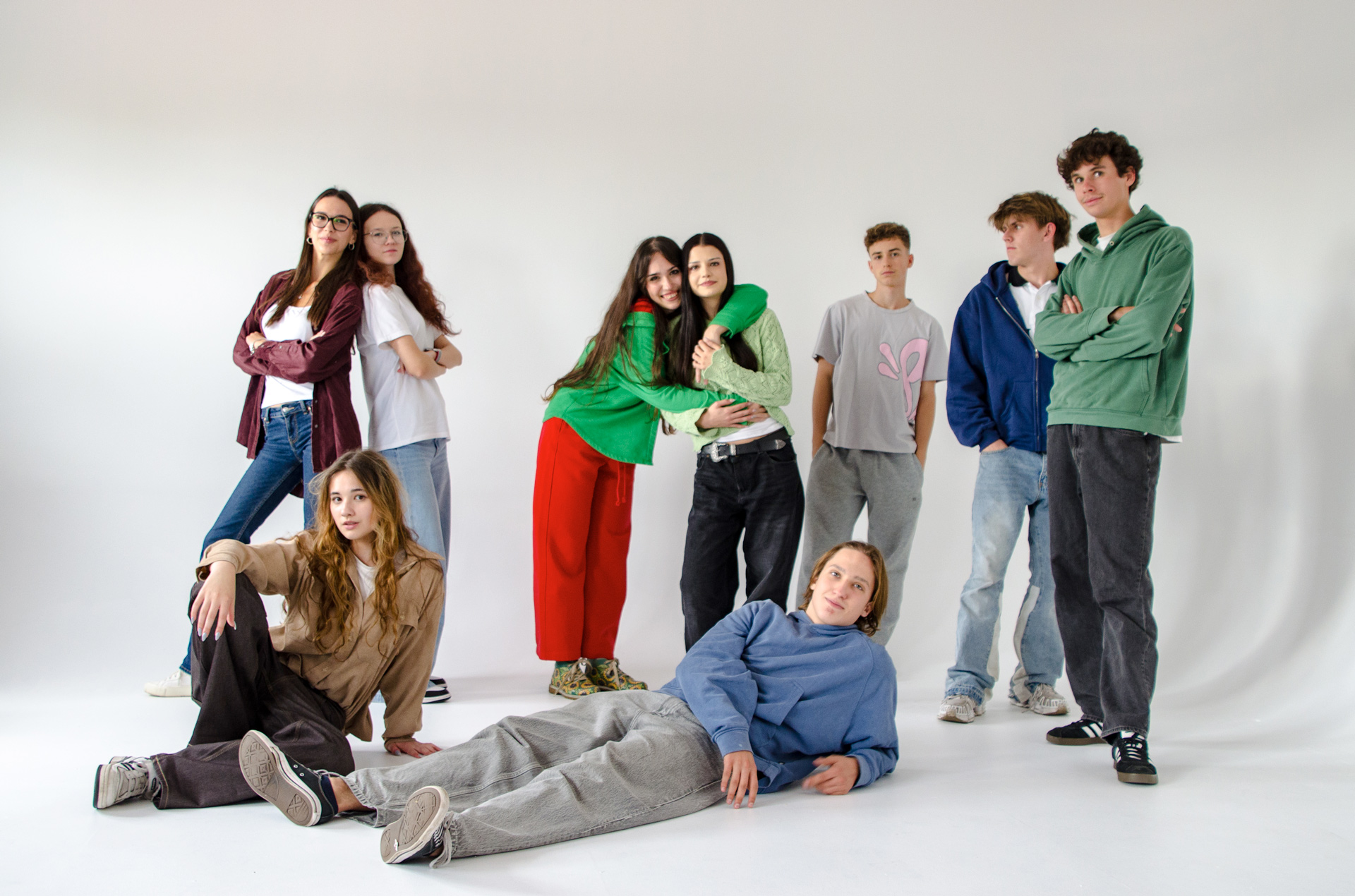 Młodzież w swobodnych pozach; leżący chłopak, siedząca na podłodze dziewczyna, przytulone dziewczyny, chłopcy z rękami w kieszeniach