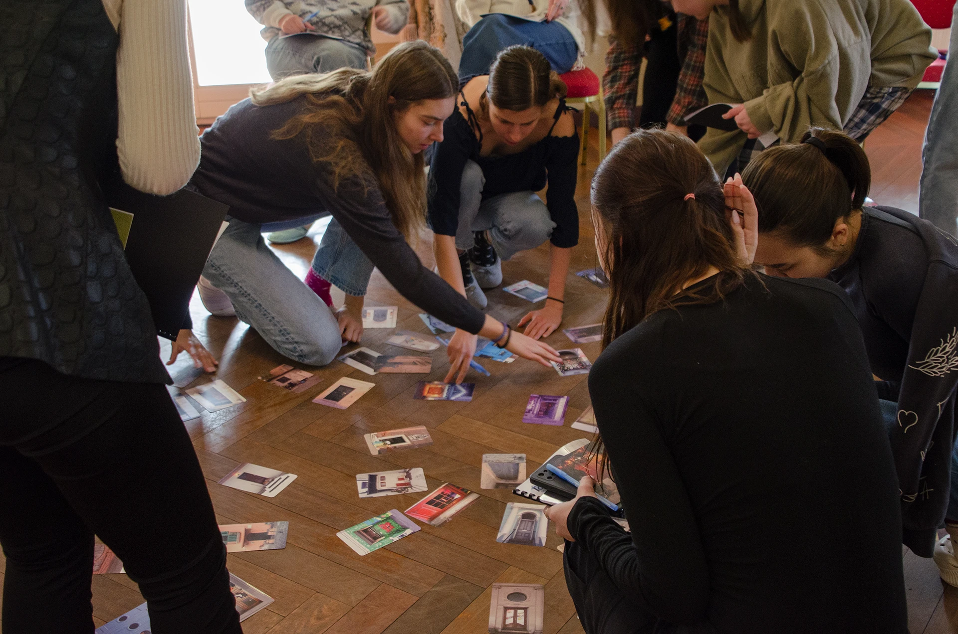 Grupa młodzieży klęczy na podłodze i rozkłada karty do gry.