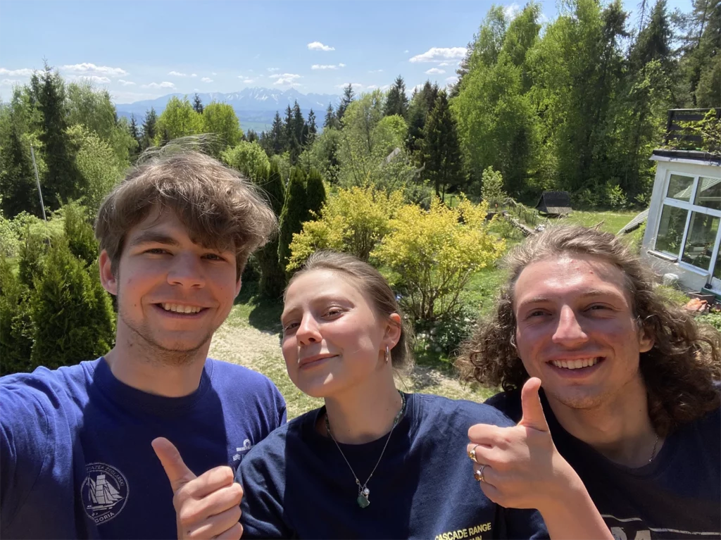 Dziewczyna i dwóch chłopaków w otoczeniu górskiej przyrody z zadowoleniem unoszą kciuki w górę.