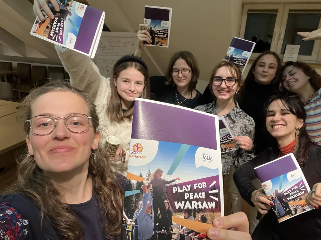 Roześmiane dziewczyny prezentują broszury Play for Peace Warsaw z logo KIKu i organizacji Play for Peace.