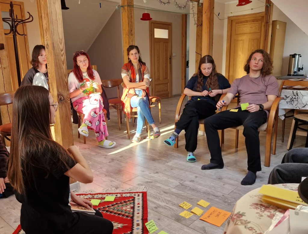 Młodzi ludzie siedzący w kręgu słuchają z uwagą prelegentki.